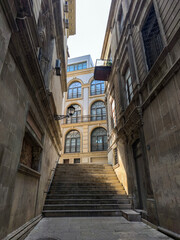 Ancient alleyway with stone stairs leading up to a classic building with arched windows and balconies, bathed in sunlight