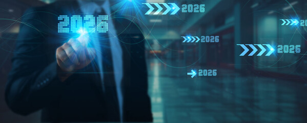 A businessman in a suit touches a futuristic digital screen displaying '2026' with progress arrows, symbolizing future business strategy, goal achievement, and corporate growth planning.