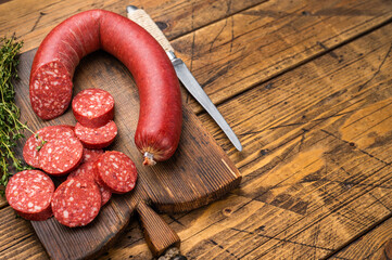 Sliced and whole Turkish sucuk (sujuk) on a rustic cutting board with thyme. Spicy dry-cured sausage, top view.
