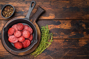 Fried Turkish sucuk (sujuk) slices in a cast iron pan with thyme and spices on a dark rustic wooden table.