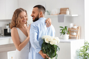 Young man with white roses for his girlfriend in kitchen