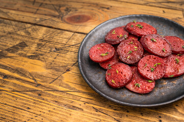 Pan-fried Turkish sucuk (sujuk) slices garnished with thyme on a dark plate. Spicy sausage breakfast or appetizer.