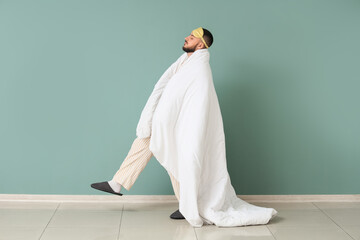 Male sleepwalker in pajamas with blanket near green wall