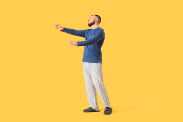 Male sleepwalker in pajamas on yellow background