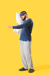 Male sleepwalker in pajamas with pillow on yellow background