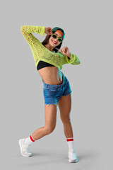 Female hip-hop dancer in cap with sunglasses on light background