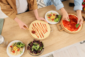 Senior woman with her grandson making pizza on table in kitchen, top view