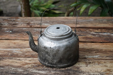 Old and weathered aluminum teapot on a rustic wooden table outdoors.