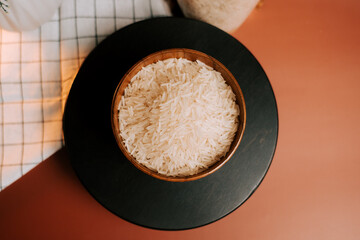 Long grain white rice in a wooden bowl on a black surface with soft light