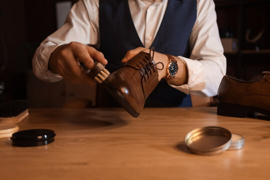 Man polishing shoe with brush at table in dark room, closeup