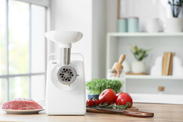 Modern meat grinder with beef and vegetables on table in kitchen