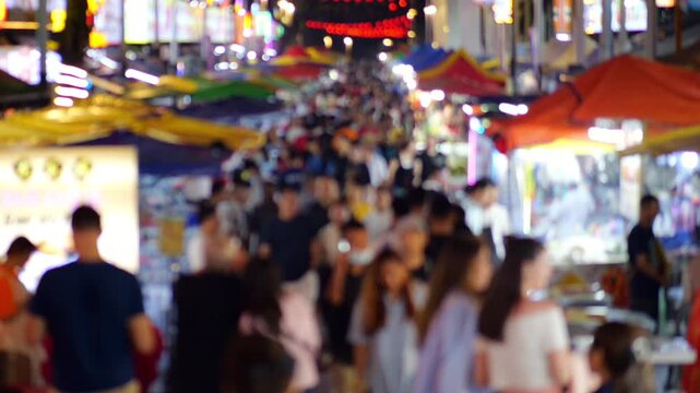 Defocused slow motion shot of crowded night food street at Bukit Bintang district, showing mass of people walking along straight alley lined with hawker stalls and restaurants.