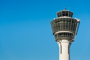 Weißer Kontrollturm (Tower) des Flughafen München MUC in der Morgensonne vor blauem wolkenlosem Himmel, Bayern, Deutschland