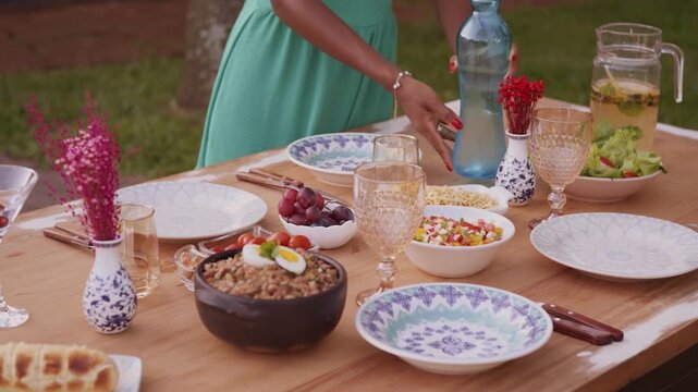 Woman Setting a Fully Loaded Lunch Table Outdoors in 4K Ultra HD &mdash; Preparing Delicious Meal Spread in Garden or Patio, Highlighting Family Gathering, Outdoor Dining, and Festive Summer Meal