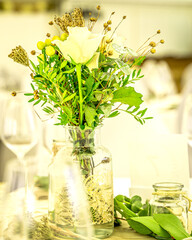 Eine helle, große Festzelt-Location ist für eine Feier festlich eingedeckt, wobei runde Tische mit strahlend weißen Tischdecken und Überwürfen über Stühlen dominieren. Die Dekoration ist in weiß-golde