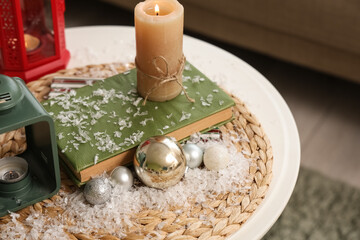 Book with candle, Christmas balls and snow on table in room, closeup