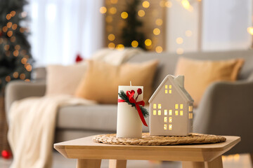 Candle with Christmas branch and house figure on table in living room