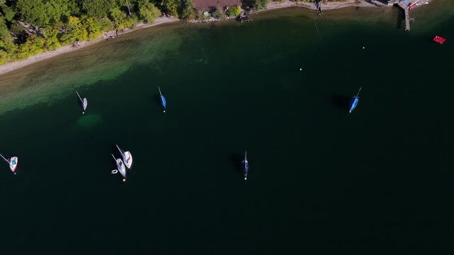 Drohnenaufnahme vom Starnberger See, Bayern, Deutschland, sonniger Herbsttag mit goldenen Baeumen, blauer Himmel, klares Wasser, Yachten und Boote am Ufer, ruhige Atmosphaere.