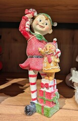 Vista de cerca de una escultura de un joven elfo de Santa Claus con paquetes de regalos en estante de comercio