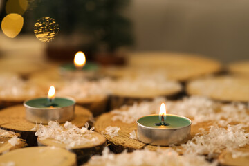 Burning candles with snow on wooden table in room decorated for Christmas, closeup