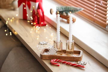 Burning candles with Christmas decor on shelf in room, closeup