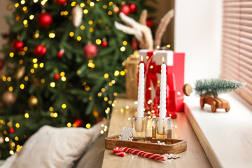 Burning candles with Christmas decor on shelf in room, closeup