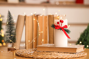 Burning candle with Christmas branches and books on table in living room, closeup