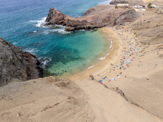 Aerial view of Playa de Papagayo in Lanzarote, Canary Islands, featuring a golden sandy beach, turquoise bay, and arid volcanic landscape.
