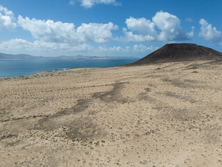 Aerial view of rugged cliffs and golden sand beach near Playa Blanca, Lanzarote, with turquoise Atlantic waters and arid volcanic terrain.
