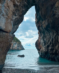 Scenic View Through Natural Rock Arch Overlooking Calm Ocean Waters and Rugged Coastline on a Cloudy Day. San Nicola Arcella, Calabria, Italy