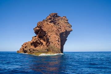 the Scandola Nature Reserve with dramatic red cliffs in the Gulf of Porto, seen from the sea under blue skies and sunshine