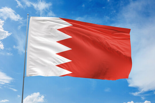 Bahrain national flag waving proudly against a bright blue sky, symbolizing unity, national pride, and cultural identity through its red field and white serrated band.