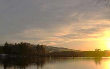 Obraz premium Sunset over calm lake with tree‑covered hills