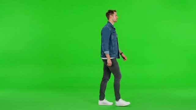 Young man in casual denim jacket walks confidently against a vibrant green screen background