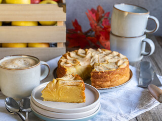 A slice of apple pie served alongside coffee, cake, and a box of organic apples in the background.