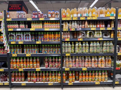 Supermarket shelves stocked with an assortment of juices and beverages in plastic bottles and cardboard cartons, including brands such as J7, Rich, Dobry, and Tropicana. Everyday retail beverage sales