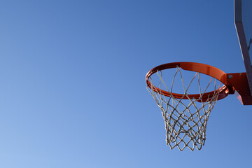 Naklejka premium Close-up of an Orange Basketball Rim and Net Against a Clear Blue Sky