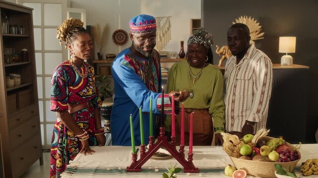 Black young man wearing traditional attire lighting seven candles symbolising principles of Kwanzaa, three positive friends watching, all joyfully clapping hands