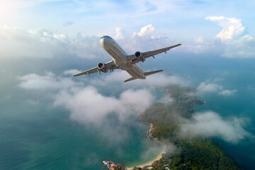 Naklejka premium Airplane jet flies above the clouds and tropical islands as it arrives at a resort on a nature-themed vacation.