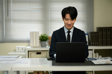 A confident banker in a suit works on a laptop, analyzing financial data and banking reports with a smile in a bright office