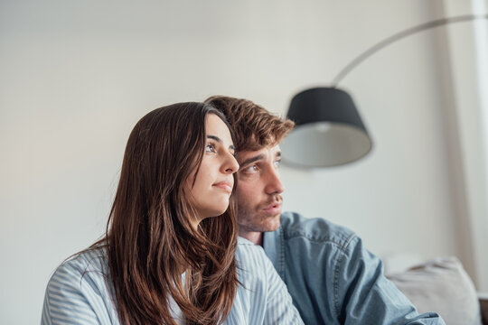 A young couple sits quietly on the sofa, worried about their future and money. Despite the stress, they find comfort and emotional support in each other’s presence at home.