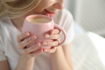 Woman with cup of cocoa drink on bed at home, closeup
