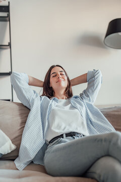Relaxed serene pretty young woman feel fatigue lounge on comfortable sofa hands behind head rest at home, happy calm lady dream enjoy wellbeing breathing fresh air in cozy home modern living room