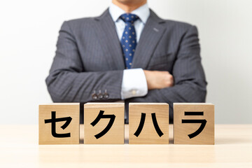 「セクハラ」と書かれたブロックと腕組みをするビジネスマン