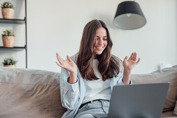 Smiling girl sit on couch at home wave talk with friend or family having video call on laptop, happy young woman greeting say hello, speak communicate using dating online application on computer