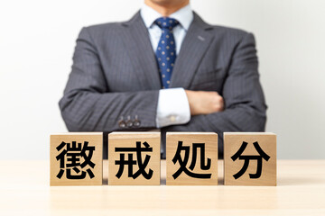 「懲戒処分」と書かれたブロックと腕組みをするビジネスマン