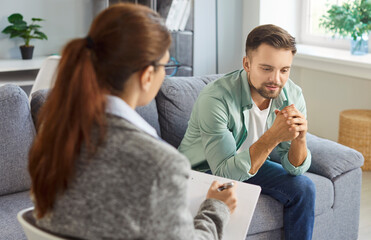 Man meeting with psychologist for counseling therapy session, talking about feelings and thoughts on consultation in office. Therapist listening, writing notes on behavior of patient