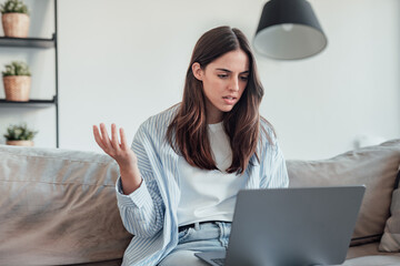 Angry young woman sit on sofa in living room frustrated having operational problems working on...