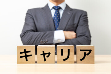 Obraz premium 「キャリア」と書かれたブロックと腕組みをするビジネスマン
