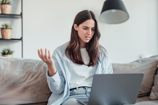 Angry young woman sit on sofa in living room frustrated having operational problems working on laptop, mad millennial girl feel stressed confused with slow internet connection or computer spam - Powered by Adobe